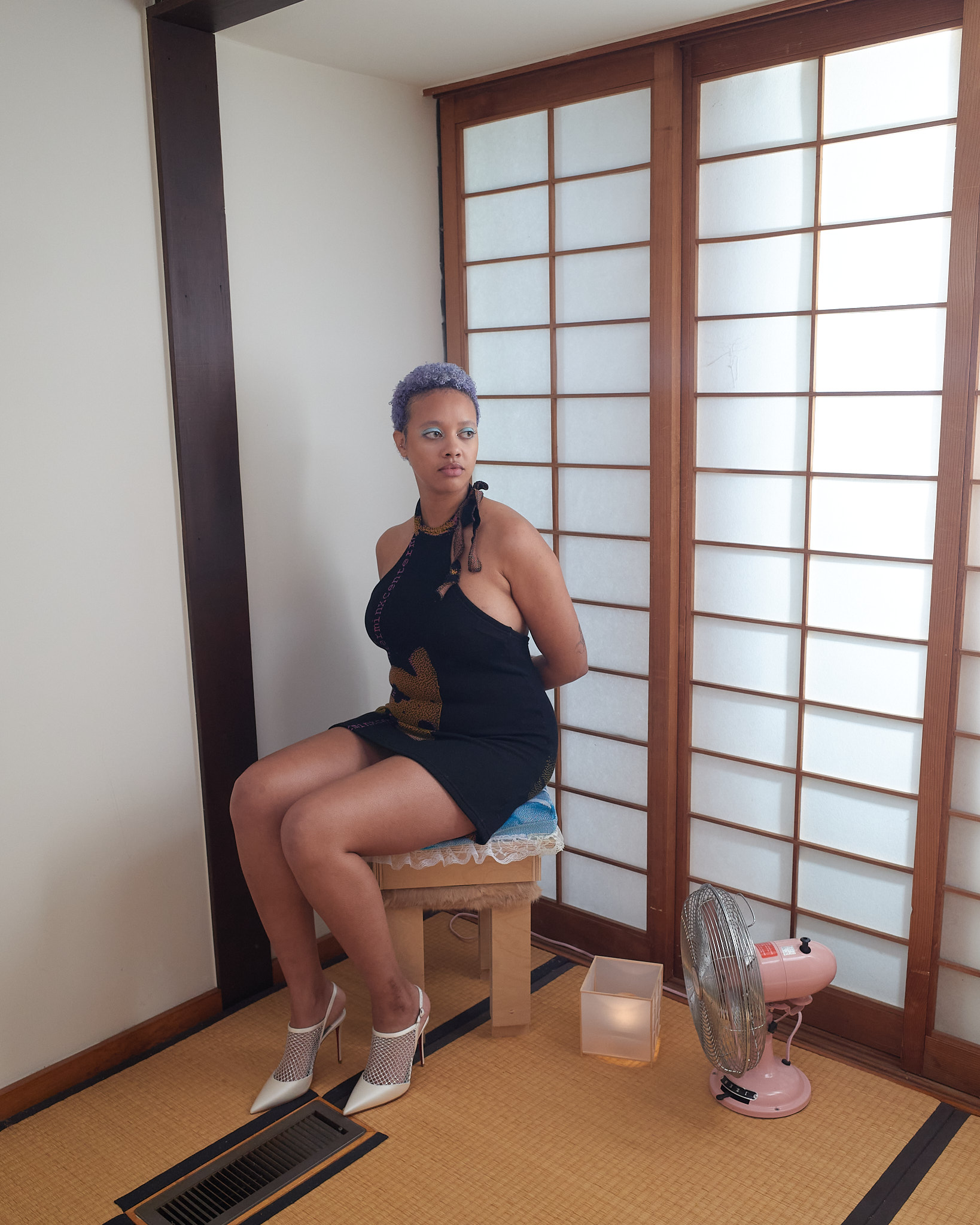 Female model sitting on a wooden stool with hands behind her back in a traditional tatami room